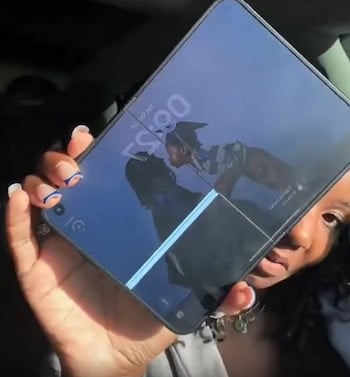 iPhone Duo: usuarios reportan grietas en la pantalla del nuevo plegable de Apple 4 Una mano sostiene un teléfono plegable abierto frente a la cámara, con una imagen en pantalla y una persona parcialmente visible detrás